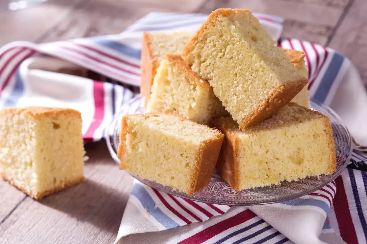 Tranches de madeira cake dor&eacute;es et moelleuses, empil&eacute;es sur une assiette en verre, avec une serviette ray&eacute;e.