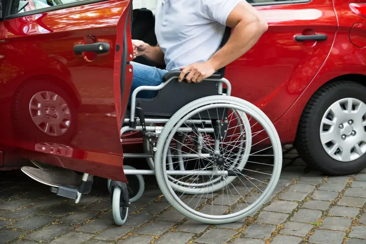 Uomo in carrozzina che sale su un'auto rossa. Informazioni su comprare auto con legge 104 a chi va intestata.