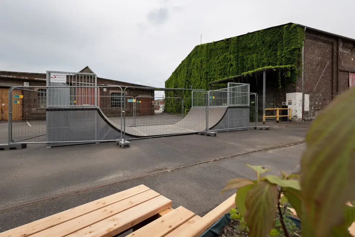 Skatepark-Elemente vor Backsteingeb&auml;uden in Bergisch Gladbach. Ein gr&uuml;ner Bewuchs bedeckt die Fassade eines Geb&auml;udes.