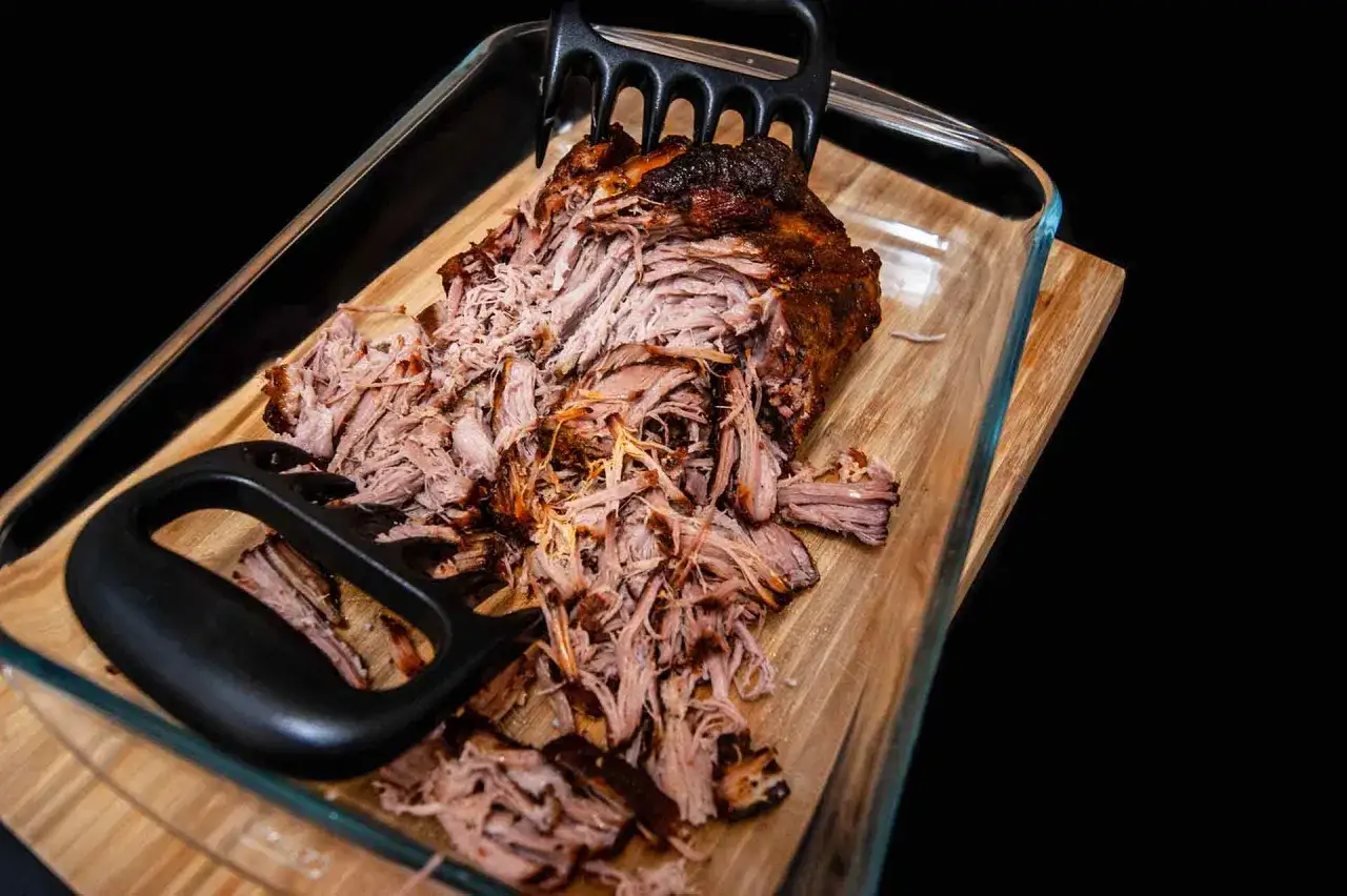 Pulled pork, frisch aus dem Backofen, wird mit Fleischkrallen zerteilt. Saftig und zart, bereit für den Genuss.