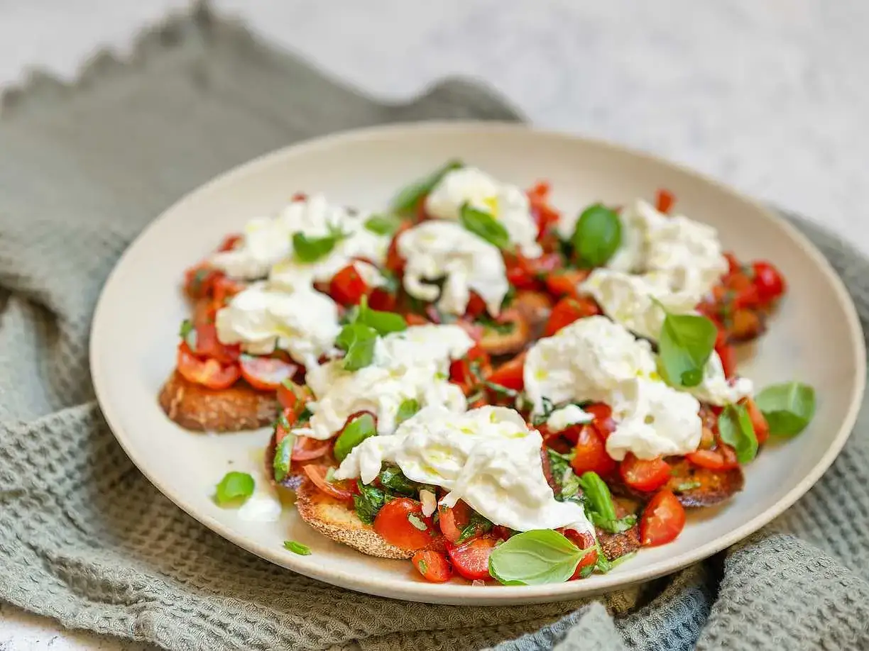 Bruschetta med burrata, färska tomater och basilika på en tallrik. En härlig sommarrätt.