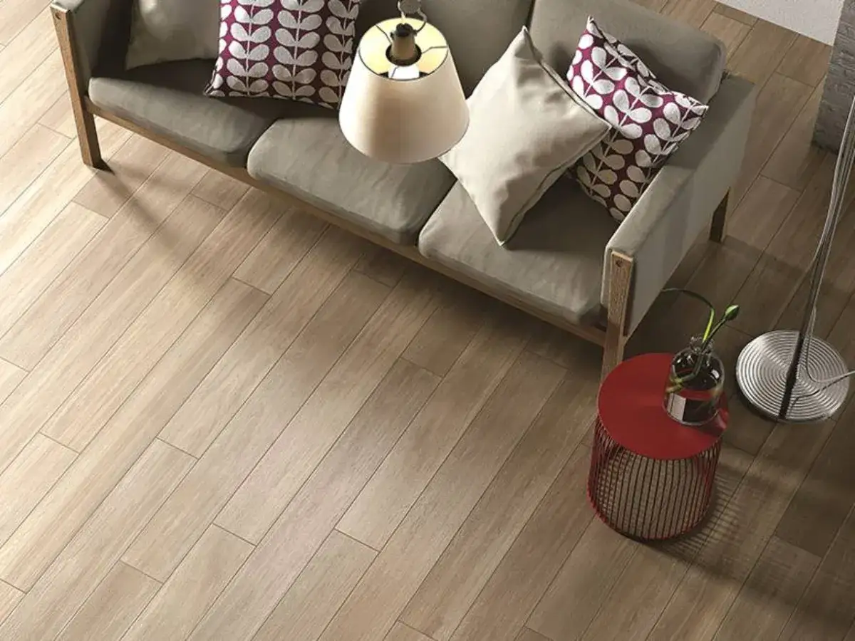 Pavimento in gres effetto legno con schemi posa a correre sfalsata, un divano grigio e un tavolino rosso.