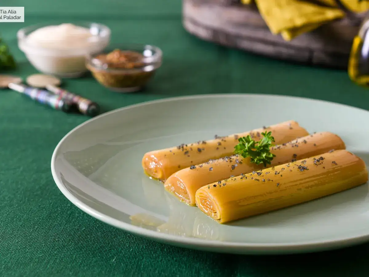 Puerros a baja temperatura, tiernos y dorados, servidos en plato verde con perejil y especias.