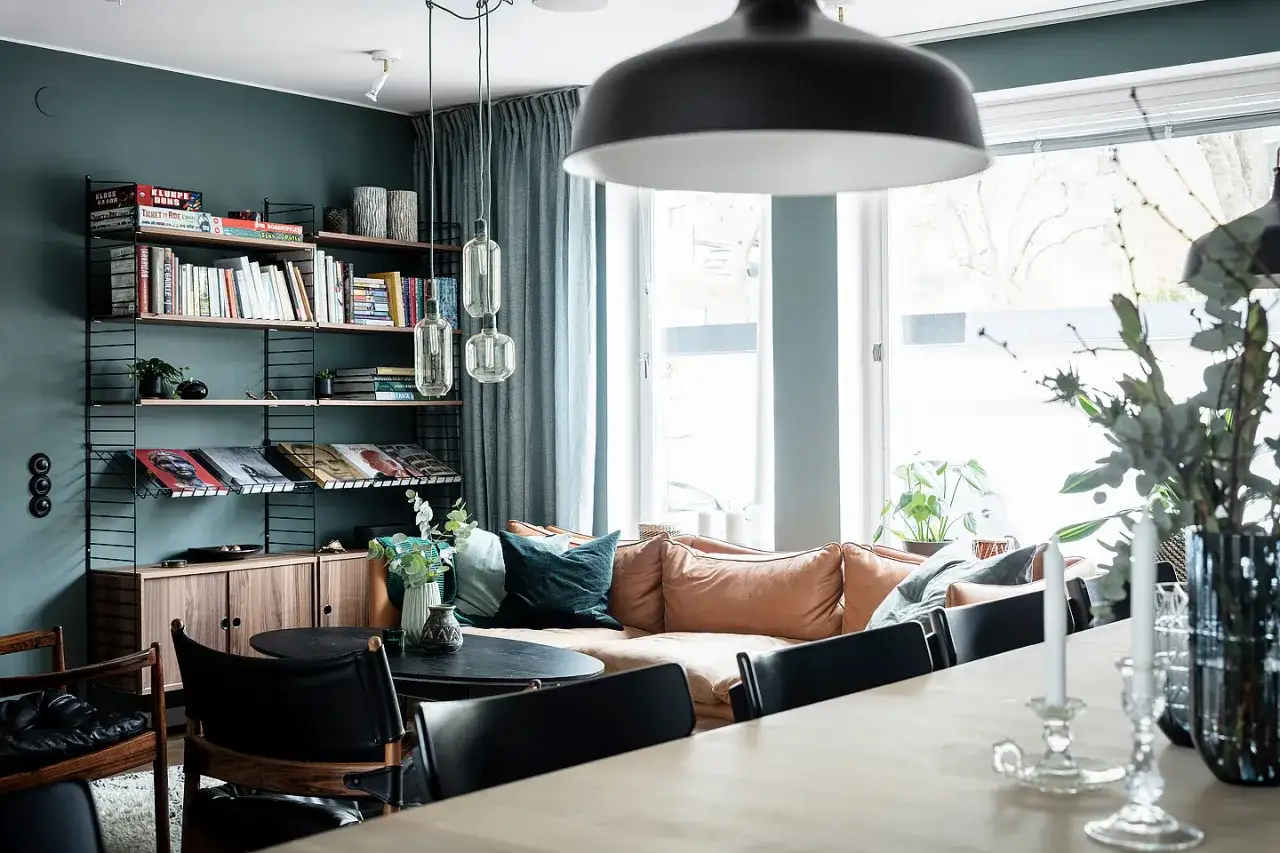 Mysigt vardagsrum i ett putsat 50-talshus med bokhylla, soffa och matplats.