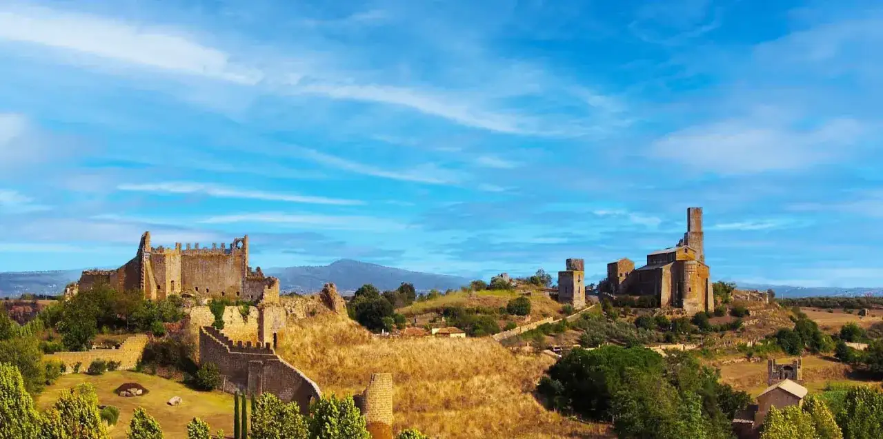 Rovine di castelli e chiese antiche si stagliano su colline aride sotto un cielo azzurro. Un paesaggio suggestivo nella riserva naturale di Tuscania.