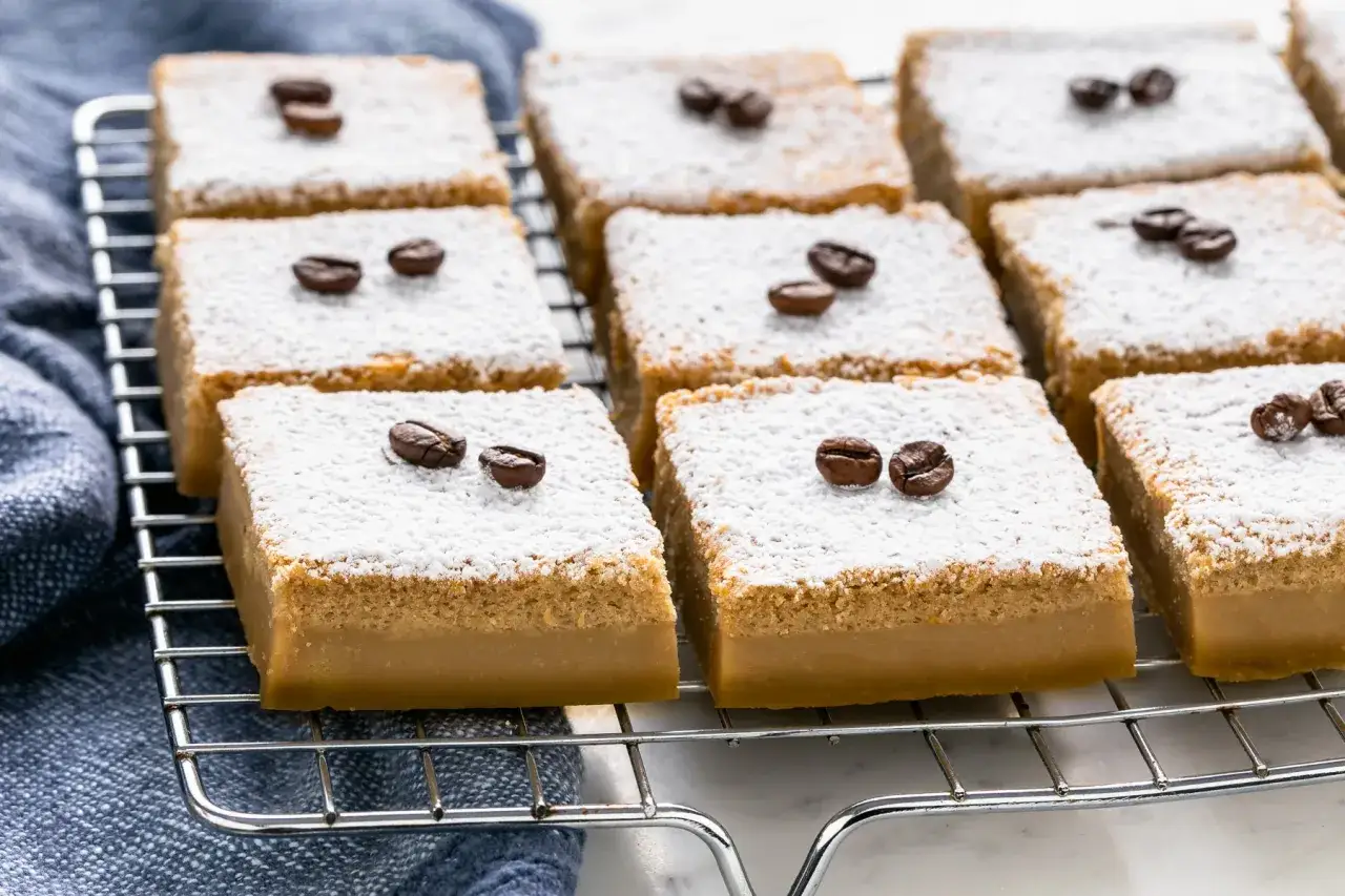Fette di torta magica al caffè, spolverate di zucchero a velo e decorate con chicchi di caffè, riposano su una griglia.