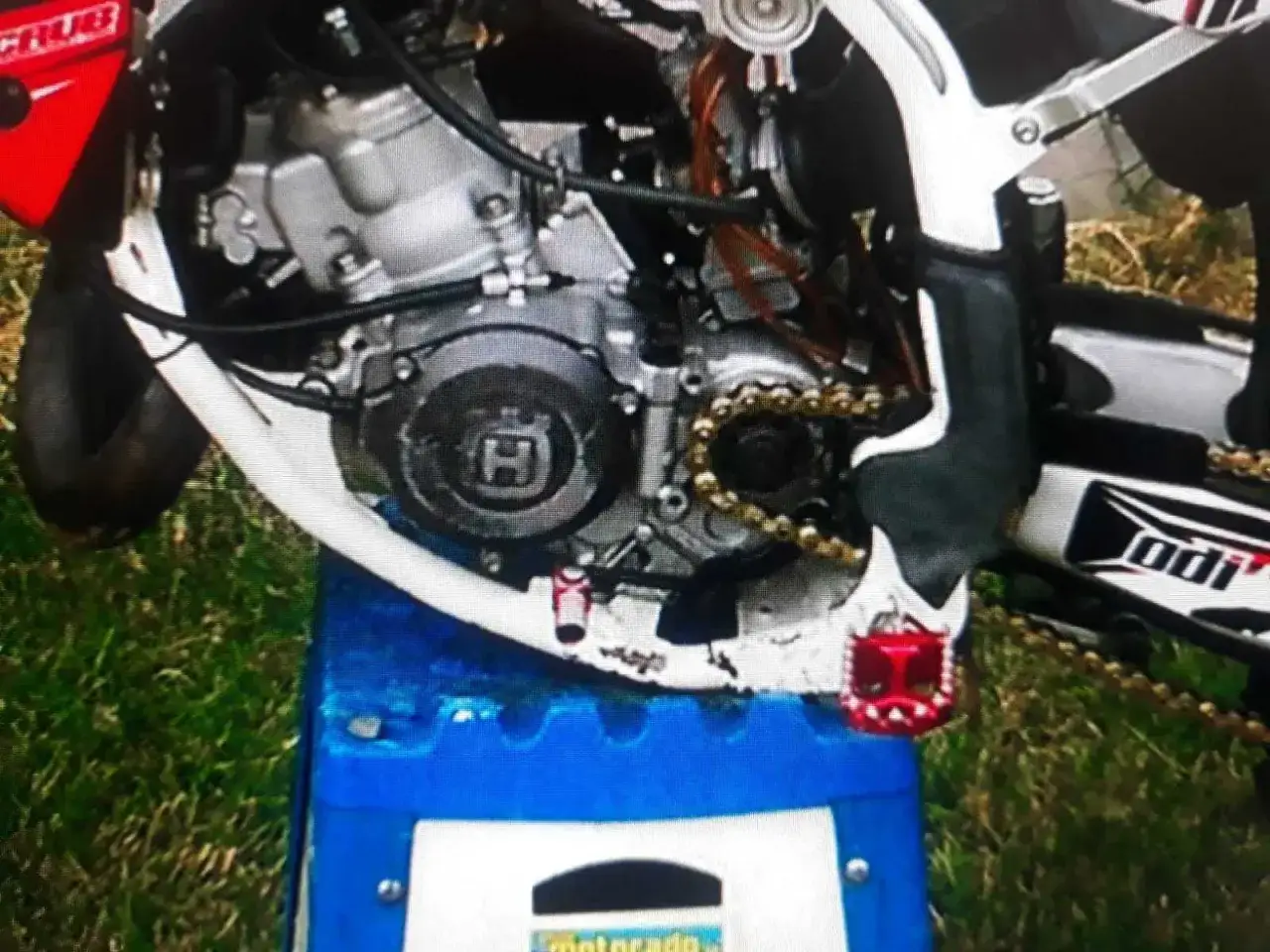 Silnik Husqvarna 125 z widocznym złotym łańcuchem i czerwonymi podn&oacute;żkami.
