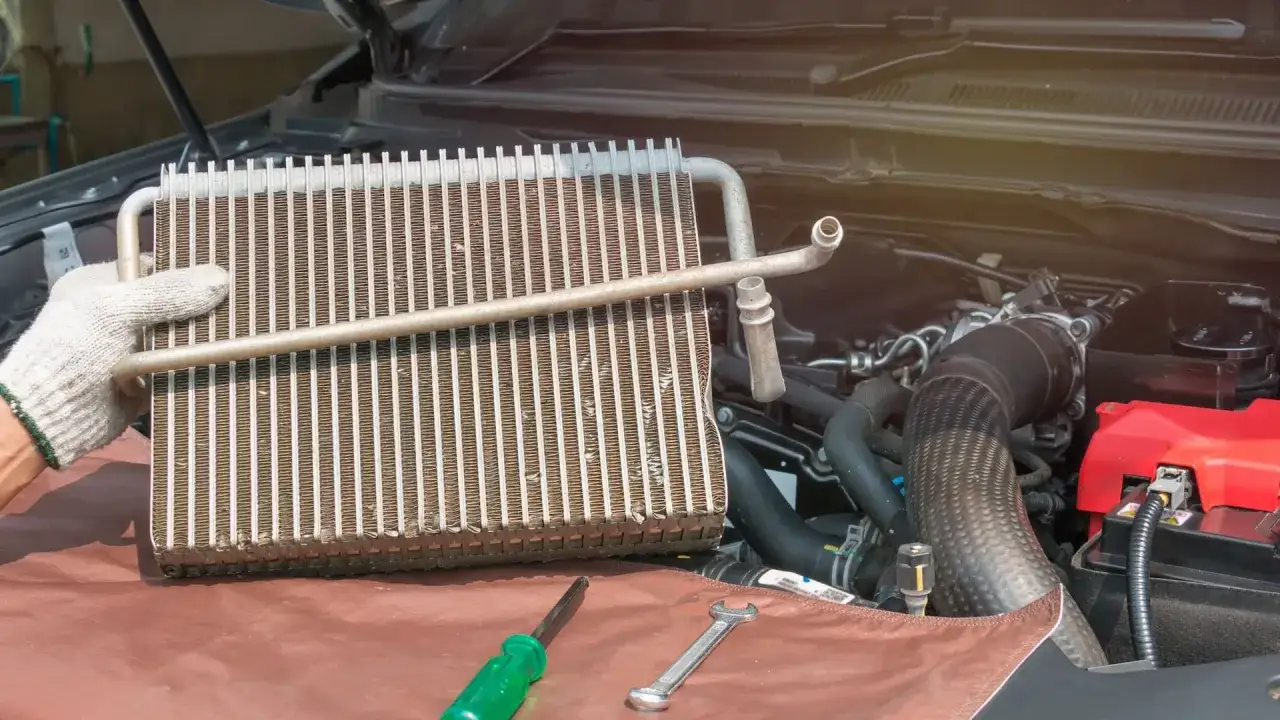 Main d'un mécanicien tenant un condenseur clim de voiture, prêt pour le remplacement. Outils à proximité.