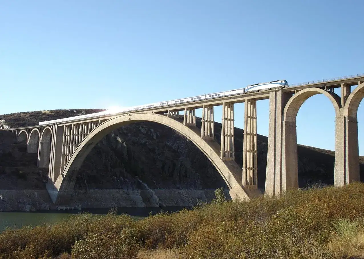 Un tren de alta velocidad cruza un imponente puente arco de hormigón sobre un valle.
