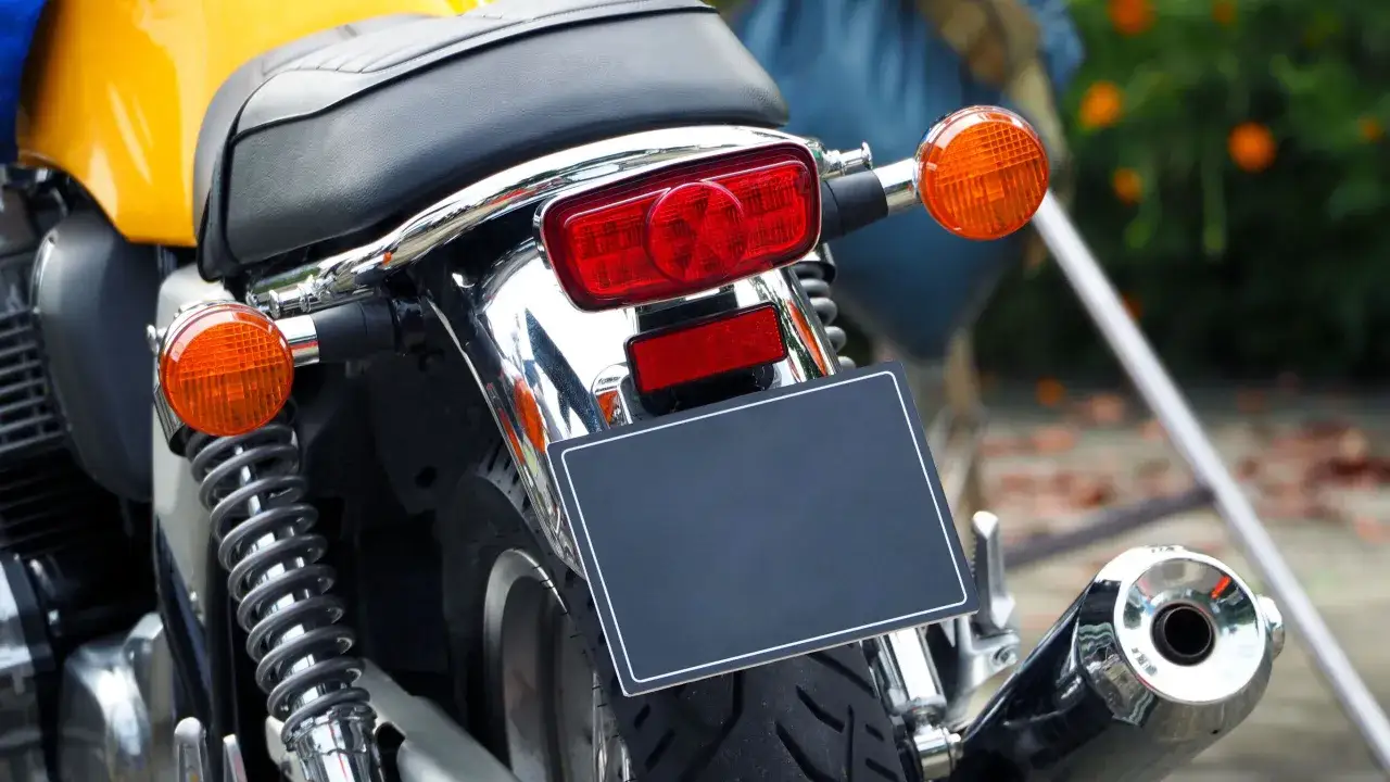 Dettaglio posteriore di una moto gialla, con targa nera vuota, luci arancioni e rosse, e scarico cromato. Un'opera d'arte su due ruote, un vero pezzo da collezione, come 100 cds.