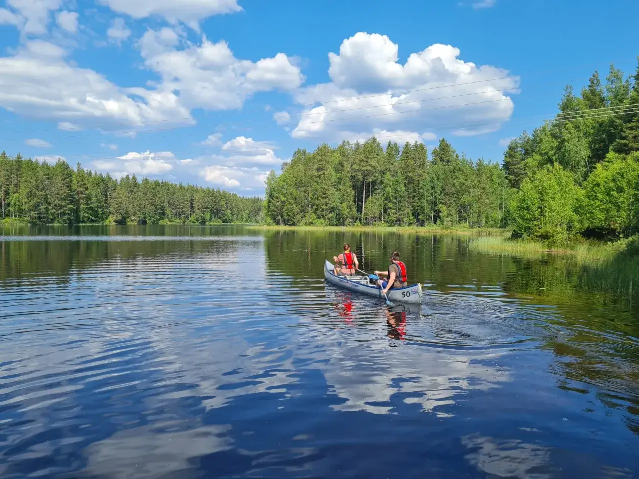 Två personer paddlar kanot på en spegelblank sjö omgivna av grönskande skog. En härlig sommardag för upplevelser i Sverige.