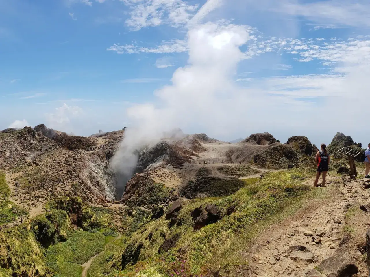 Vue panoramique d'une montagne en Guadeloupe, avec un cratère fumant et des randonneurs admirant le paysage volcanique.