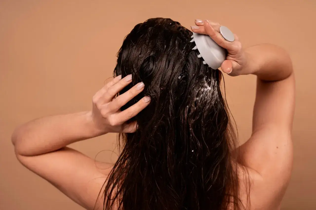 Kobieta masuje skórę głowy, aplikując peeling do włosów.