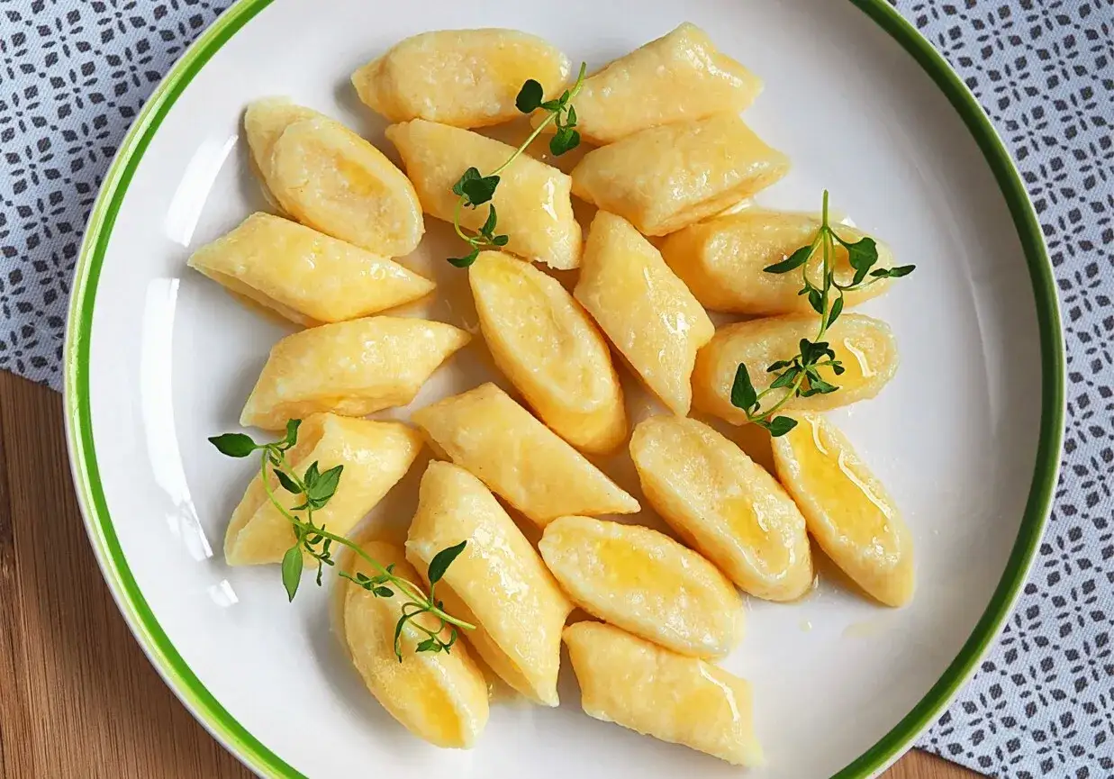 Pyszne, domowe kluski leniwe polane masłem, ozdobione gałązkami świeżego tymianku.