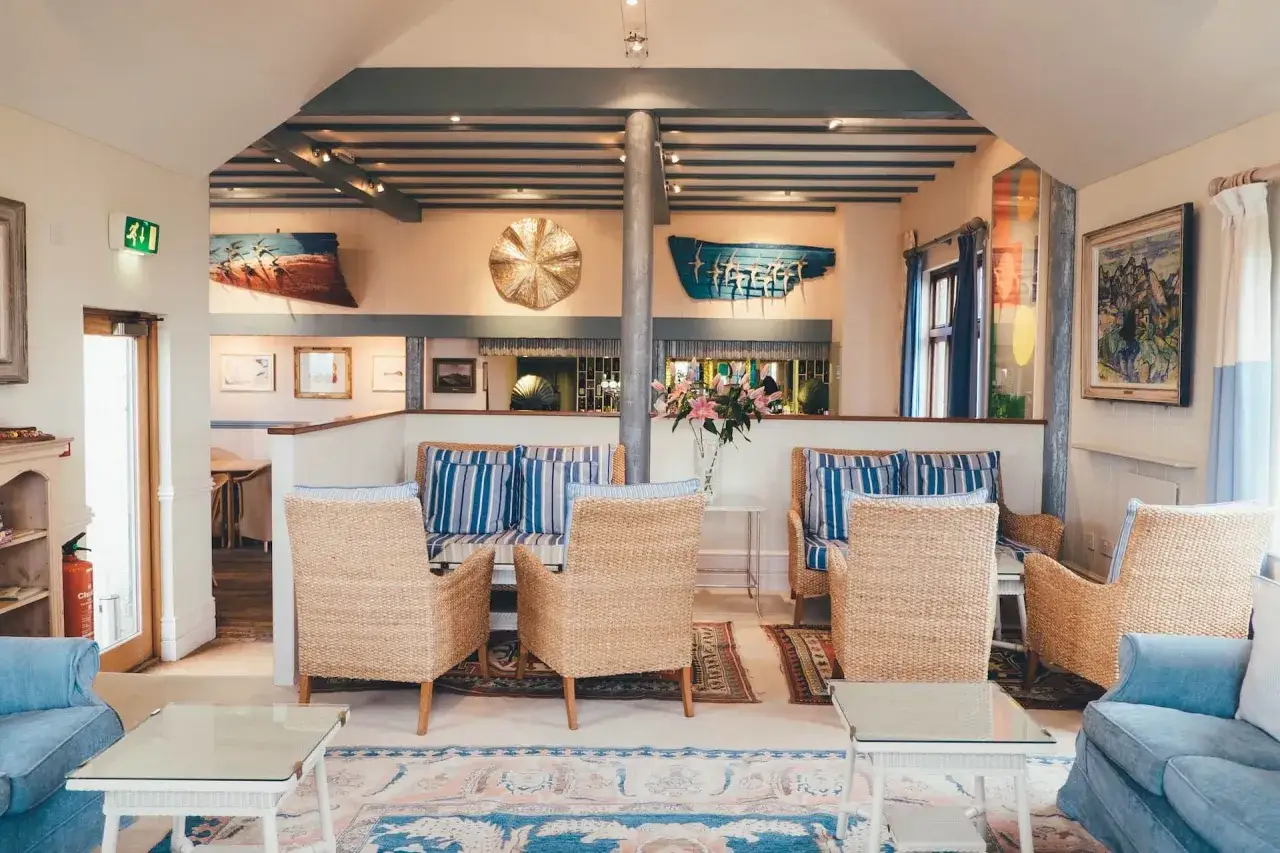 Un salotto con arredamento coastal: sedie in vimini, divani blu a righe, tappeti orientali e quadri a tema marino creano un'atmosfera rilassante.