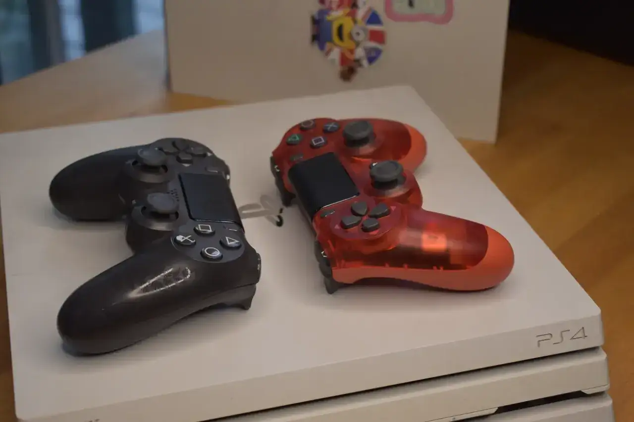 Dwa kontrolery, czarny i czerwony, leżą na białej konsoli PS4. Pamiętasz, w którym roku wyszło PS4?