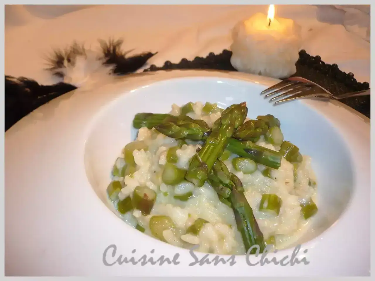 Un crémeux risotto aux asperges, garni de pointes vertes croquantes, servi dans un bol blanc, avec une bougie allumée en arrière-plan.