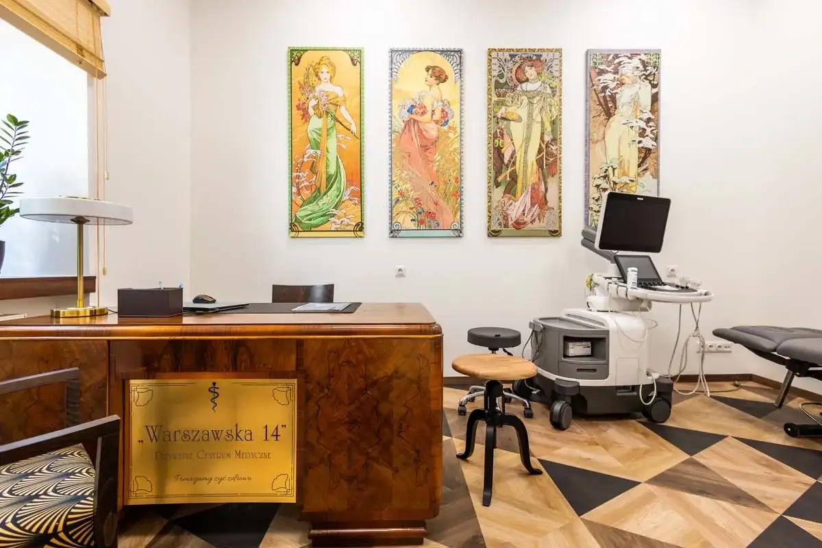 Gabinet lekarski z obrazami w stylu Art Nouveau, biurkiem i aparaturą medyczną.