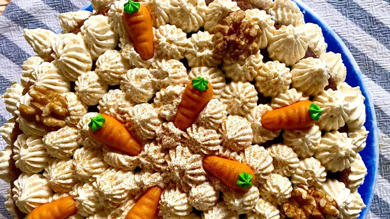 Deliciosa tarta de zanahoria y coco, decorada con zanahorias de mazapán, nueces y crema batida.