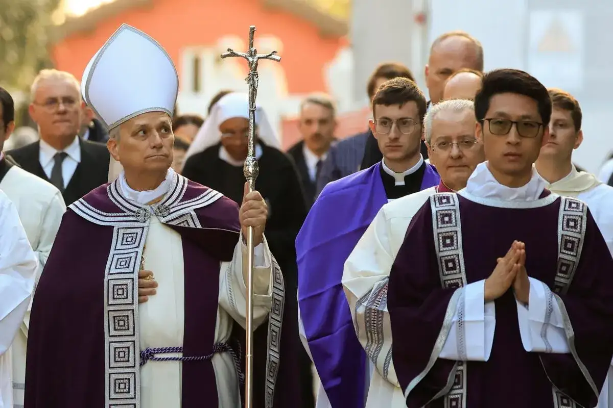 Clergy in purple vestments, a bishop holding a crucifix, walk in procession, marking a solemn scripture for Ash Wednesday.