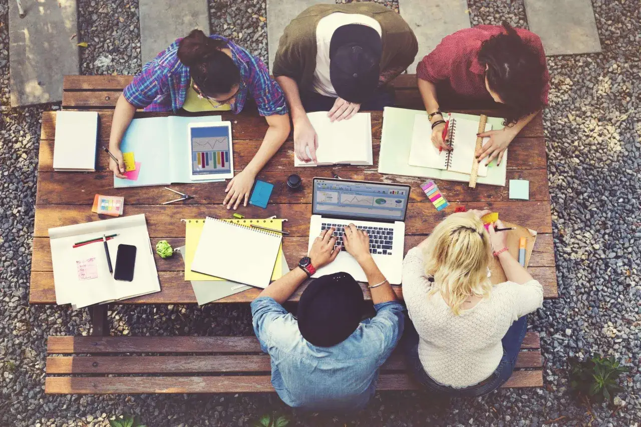 Fünf junge Leute lernen draußen. Sie arbeiten an Laptops und Notizbüchern, vielleicht für ein sprachreise stipendium.