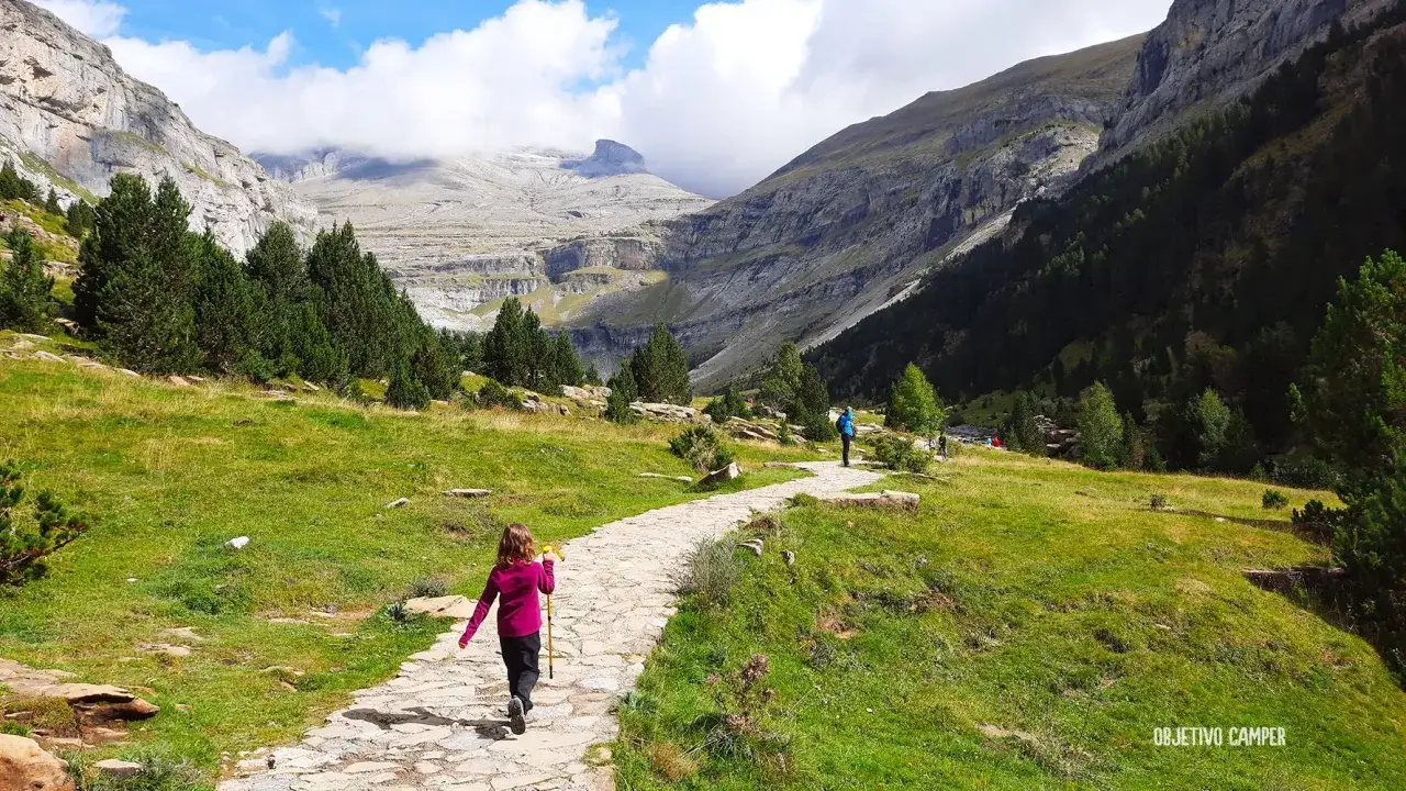 Niños explorando el sendero de Ordesa y Monte Perdido, rodeados de imponentes montañas y vegetación verde.