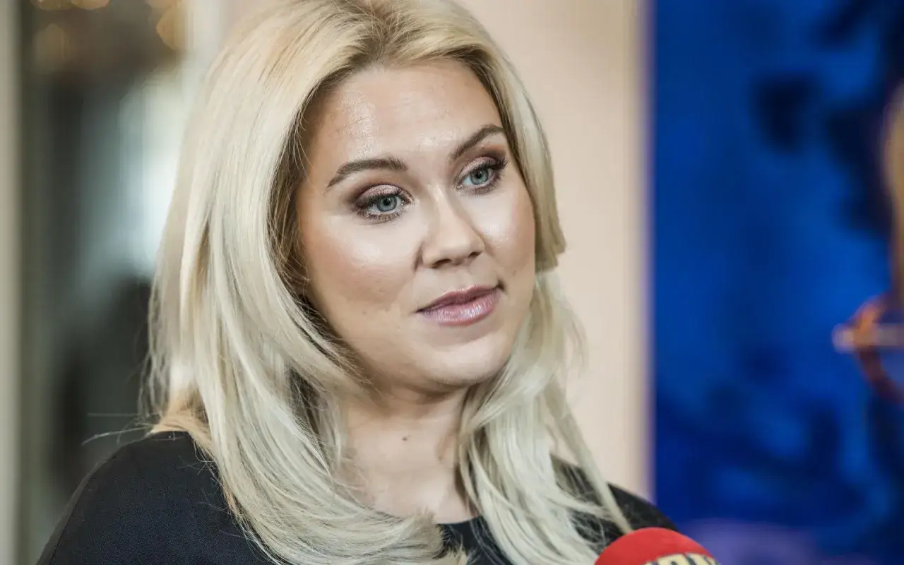 Caroline Hainer, med blont h&aring;r och makeup, ser &aring;t sidan. En mikrofon syns i f&ouml;rgrunden.