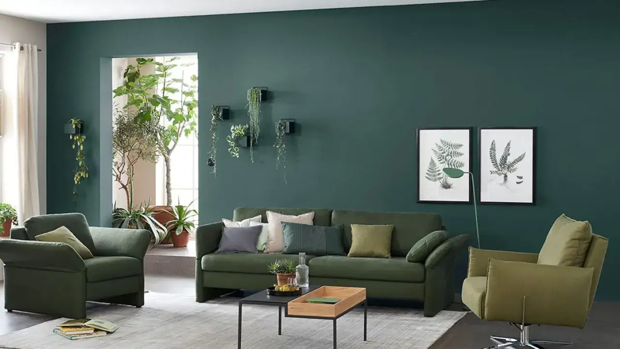 Grünes Wohnzimmer mit bequemen Sofas und Sesseln. Die Wände sind in einem tiefen Grünton gestrichen, der an die Natur erinnert. Pflanzen zieren die Wände und den Raum, was die Frage