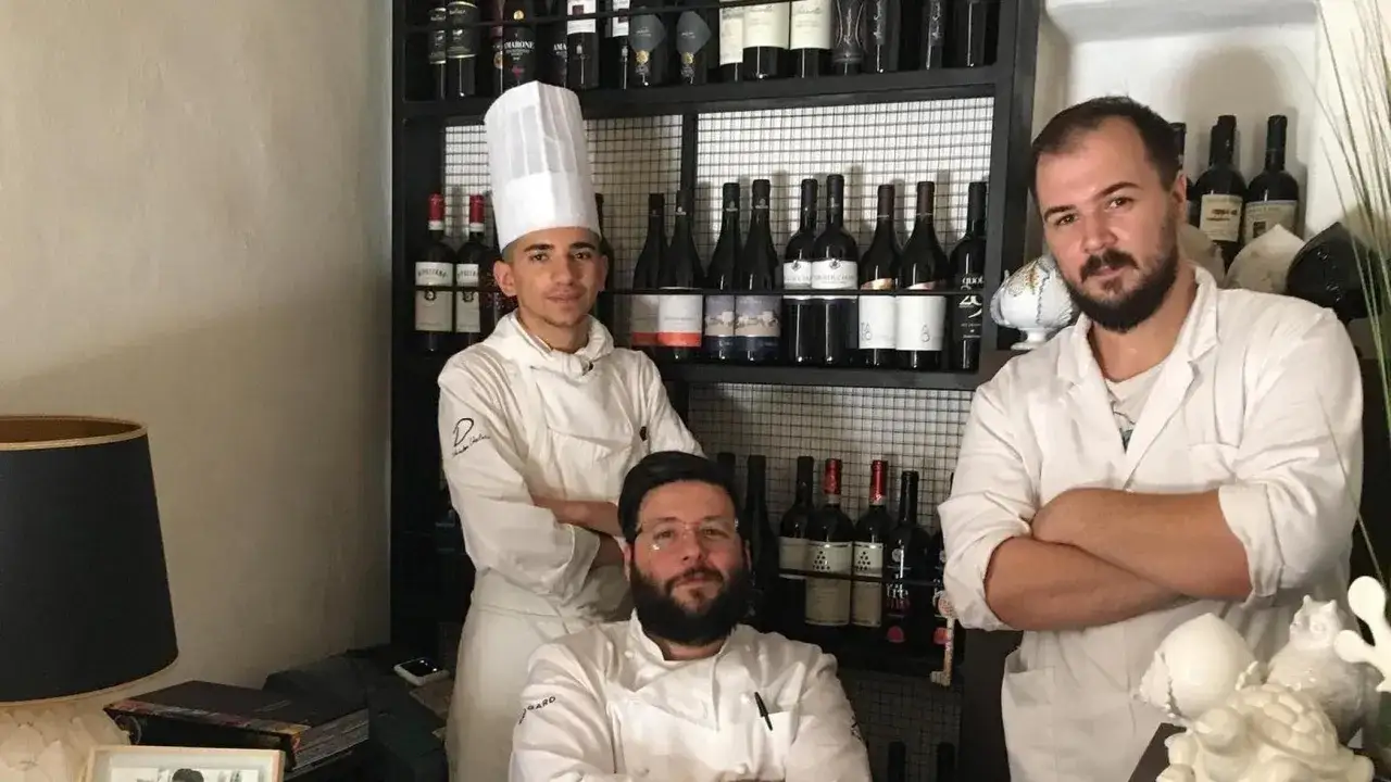 Tre chef posano davanti a una cantina di vini, pronti a servire i migliori ristoranti stellati Puglia.