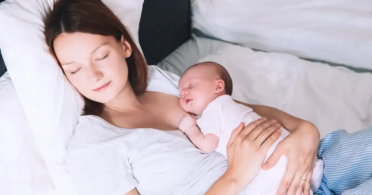 Matka odpoczywa z dzieckiem na rękach. To spokojny czas połogu, pełen czułości i bliskości.
