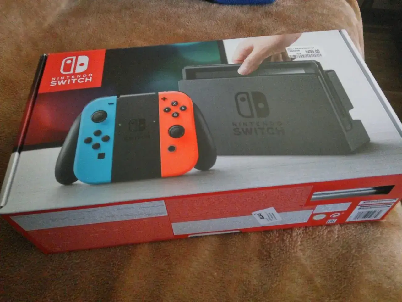 Pudełko z konsolą Nintendo Switch, z widocznymi kontrolerami Joy-Con w kolorach niebieskim i pomarańczowym.
