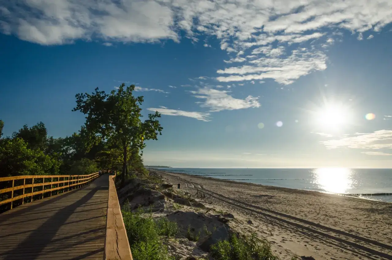 Drewniana ścieżka wzdłuż plaży, idealna infrastruktura rowerowa. Słońce odbija się w morzu, tworząc piękny widok.