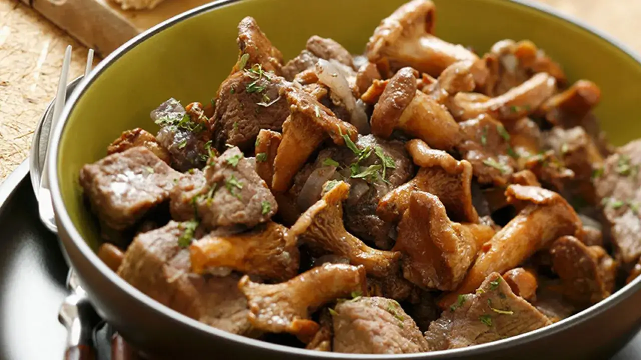 Un tazón de boeuf bourguignon con trozos de carne tierna y champiñones dorados, adornado con hierbas frescas.