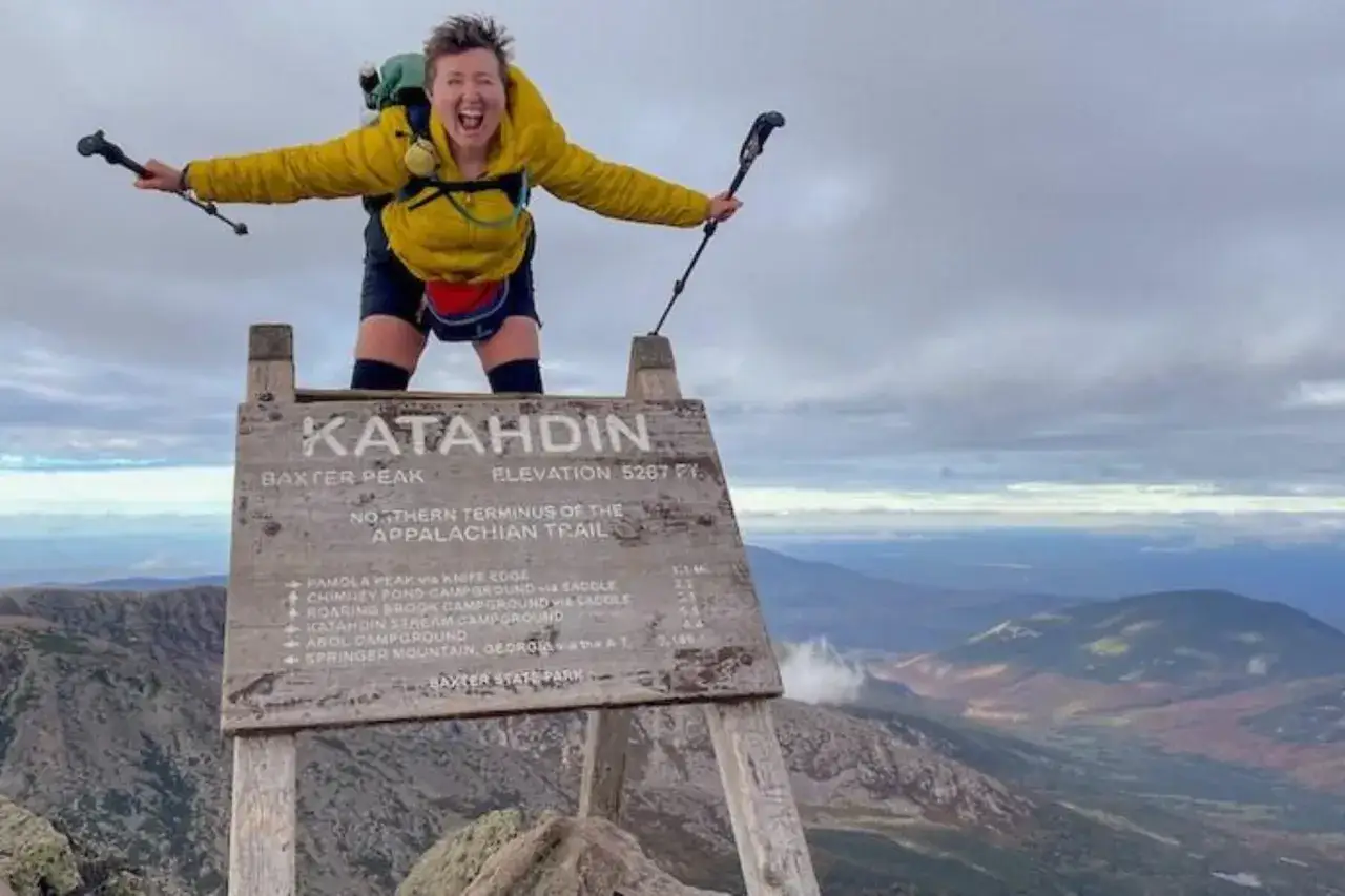 Joyful hiker celebrates completing a thru hiking journey on Katahdin, the northern terminus of the Appalachian Trail.