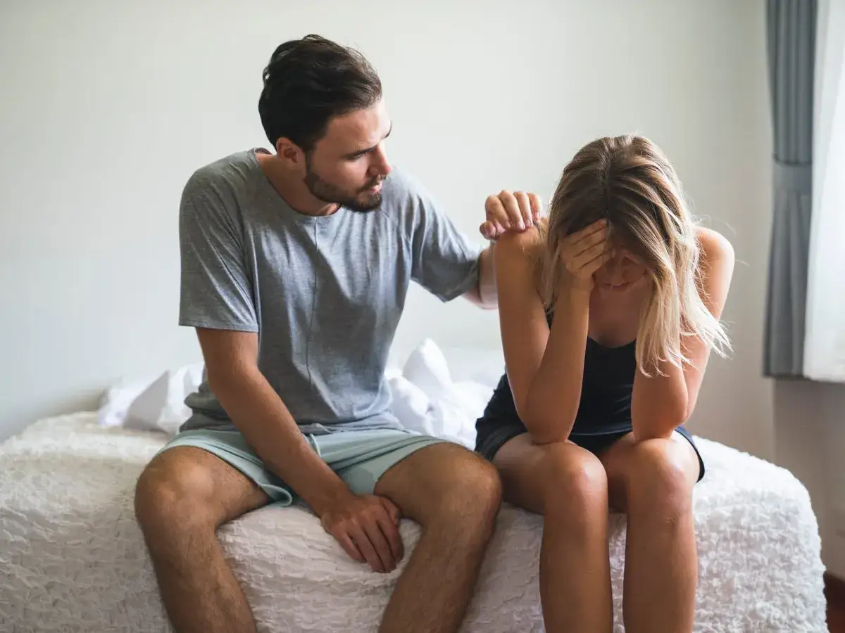Hombre consuela a su pareja, que llora en la cama. Ella parece haber tenido un mal sueño, quizás soñar que tu pareja tontea con otra.