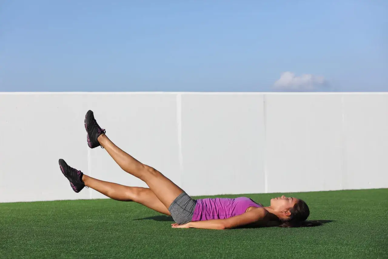 Femme effectuant un exercice bas du ventre, jambes levées, sur une pelouse artificielle.