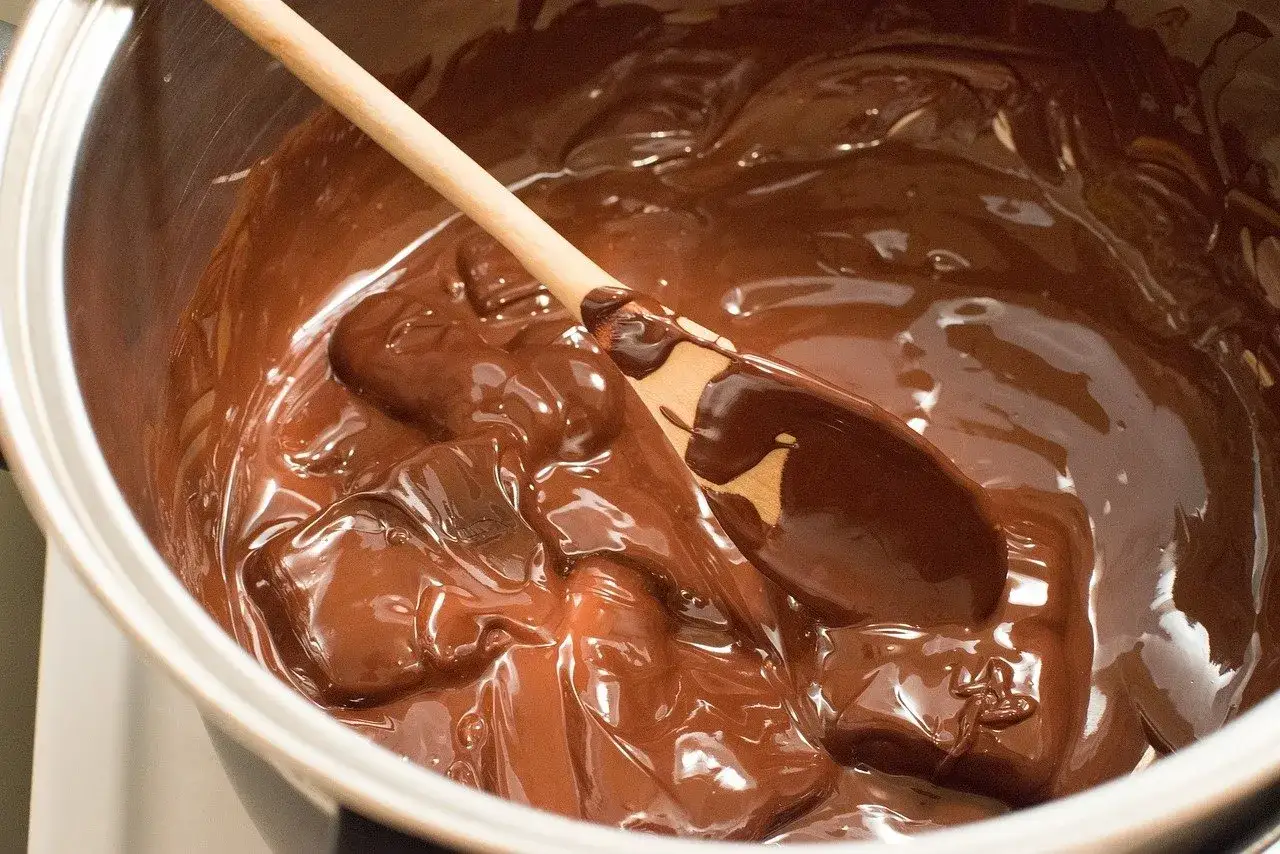 Cuchara de madera removiendo chocolate derretido en una olla. El proceso de como derretir chocolate es sencillo y delicioso.