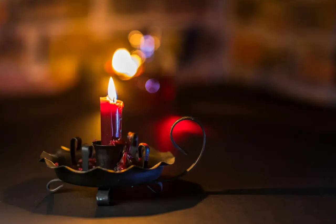 A single red candle burns in a dark, ornate holder, casting a warm glow. The flickering flame evokes a sense of peace, perhaps during an end of life prayer.