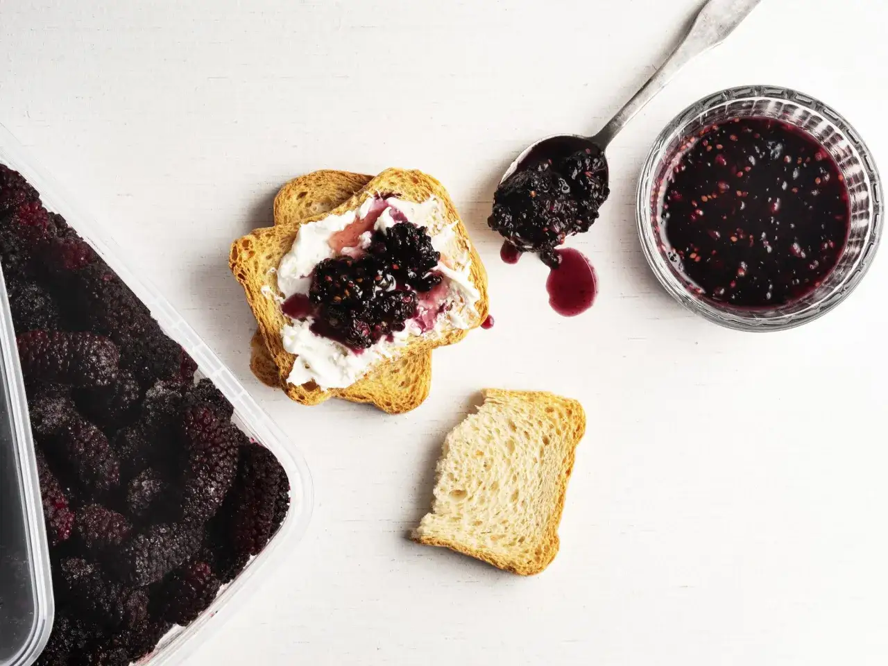 Fetta biscottata con ricotta e marmellata di more, come nella ricetta marmellata di more fatto in casa da Benedetta. Accanto, un contenitore di more fresche e un cucchiaio con la marmellata.