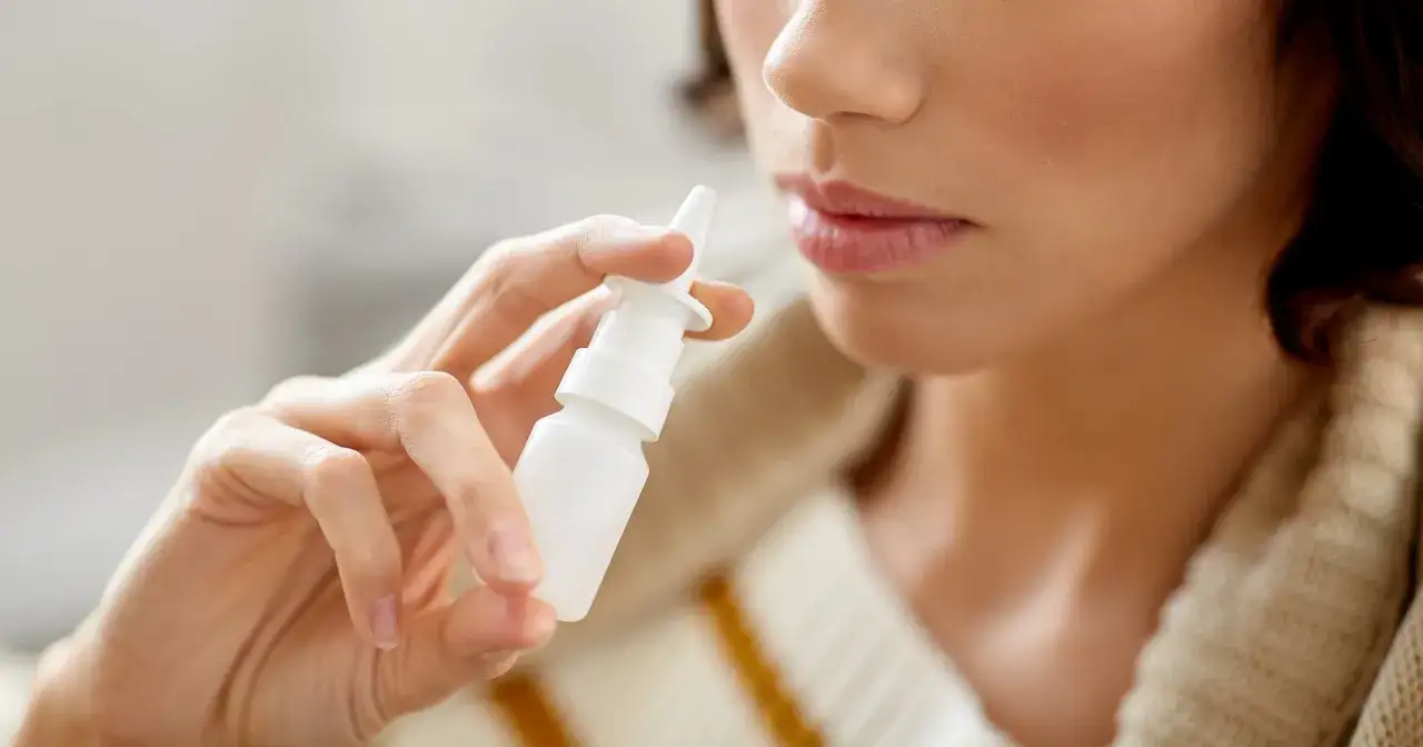 Kobieta trzyma biały spray do nosa, być może Septanazal, aby złagodzić zatkany nos.