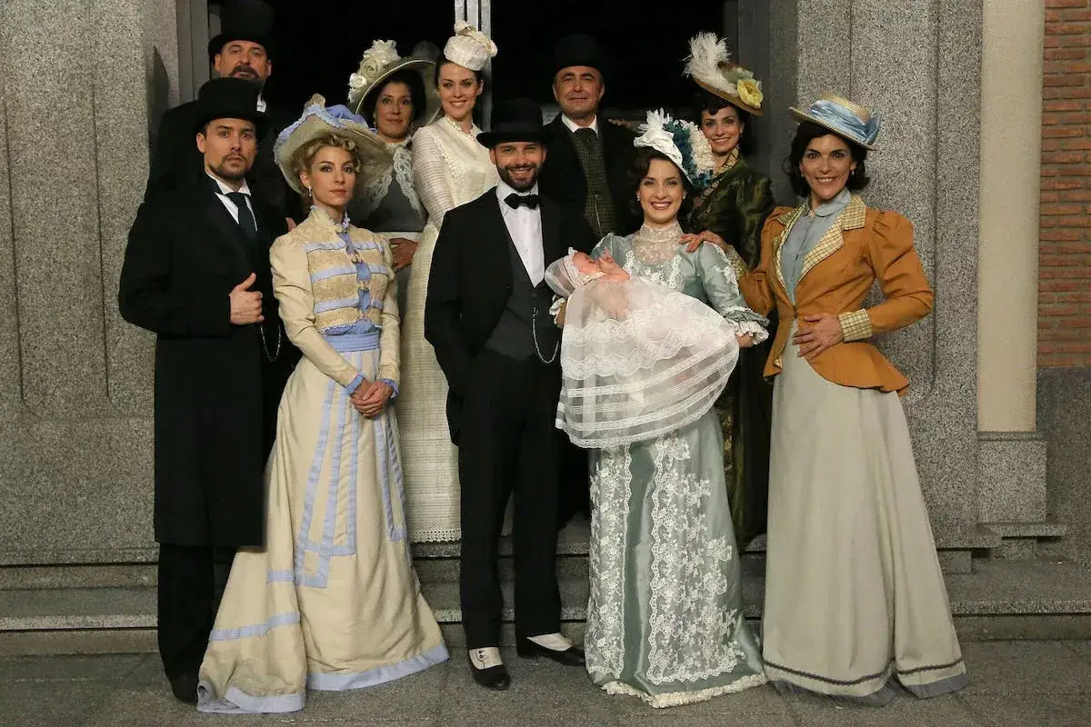 Un gruppo di persone in abiti d'epoca, con un neonato in braccio, anticipazioni una vita di famiglia e di stile.