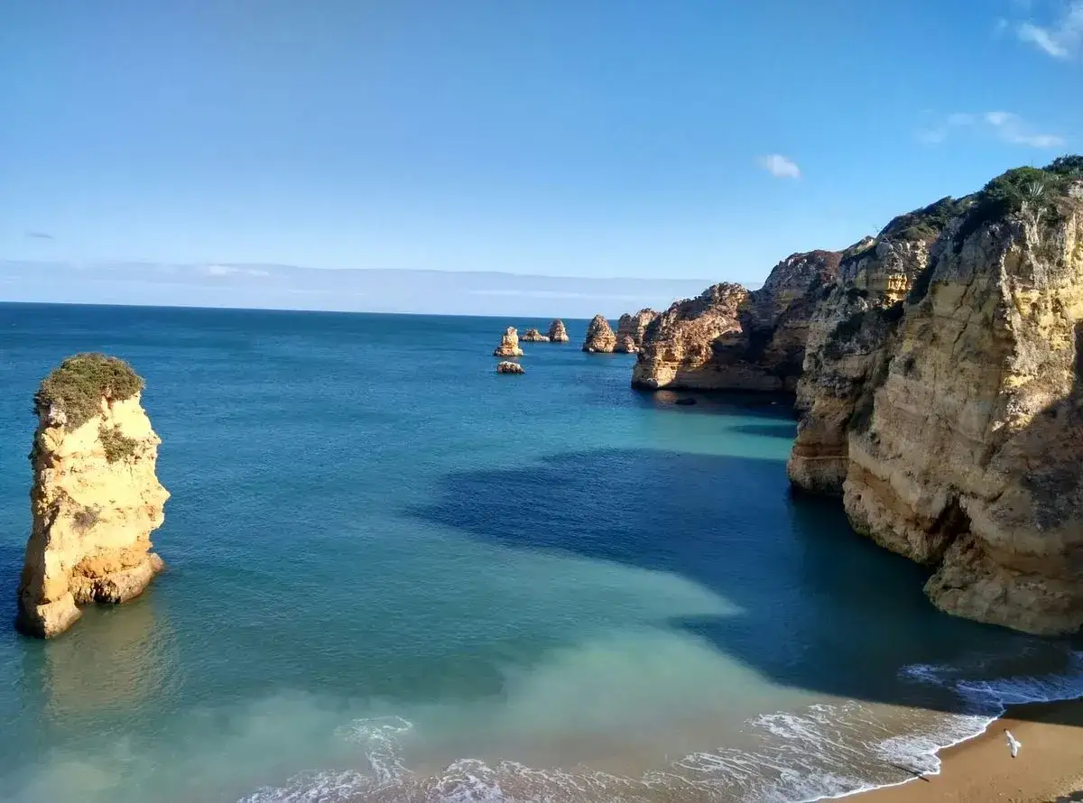 Felsformationen ragen aus dem türkisfarbenen Wasser am Praia de Alvor. Die Sonne beleuchtet die Klippen und das Meer.