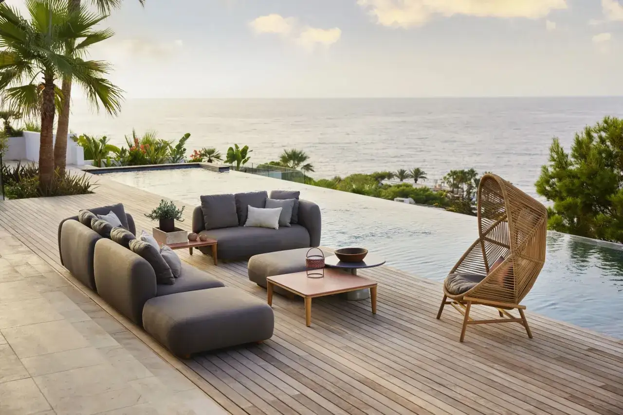 Sofás modulares y sillón de mimbre en patios modernos junto a una piscina infinita con vistas al mar.