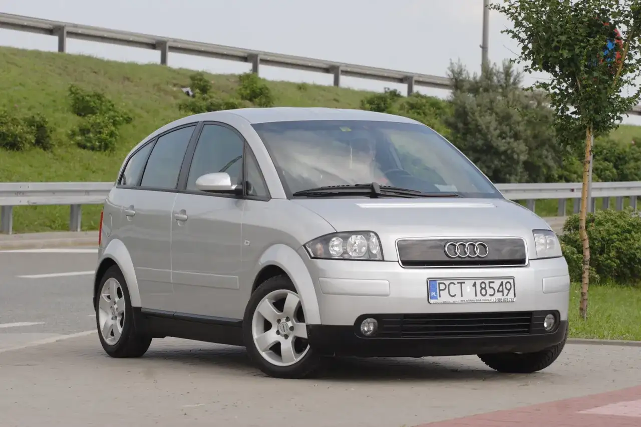 Srebrne Audi A2, kompaktowe auto miejskie, zaparkowane na chodniku.