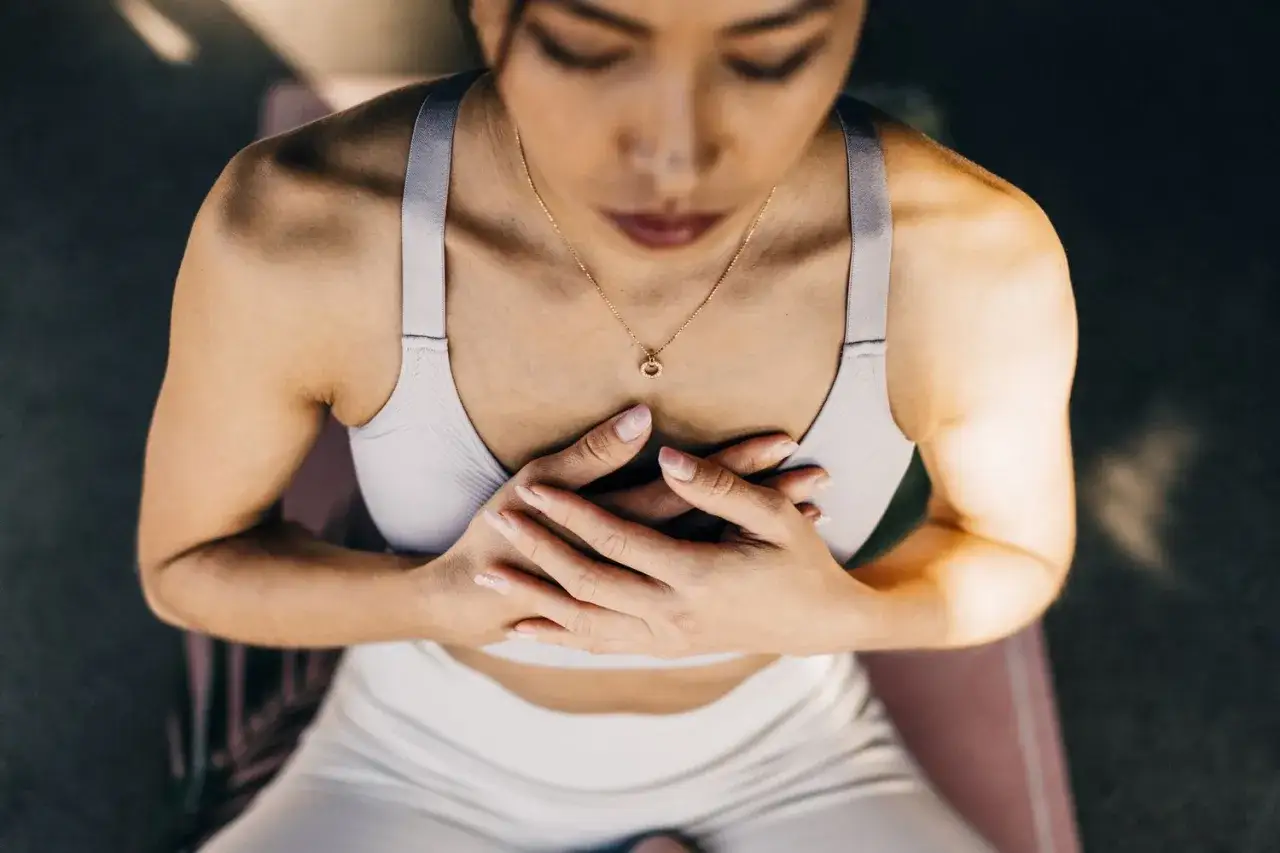 Femme en tenue de sport, mains sur le c&oelig;ur, m&eacute;ditant. D&eacute;couvrez les 7 bienfaits de la respiration abdominale pour le bien-&ecirc;tre.