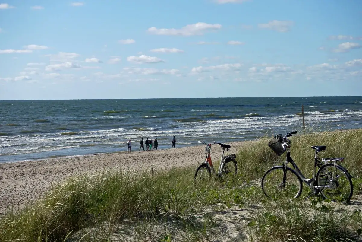 Dwa rowery na piaszczystej plaży, w tle Bałtyk i spacerujący ludzie. To piękny łotewski port nad bałtykiem.