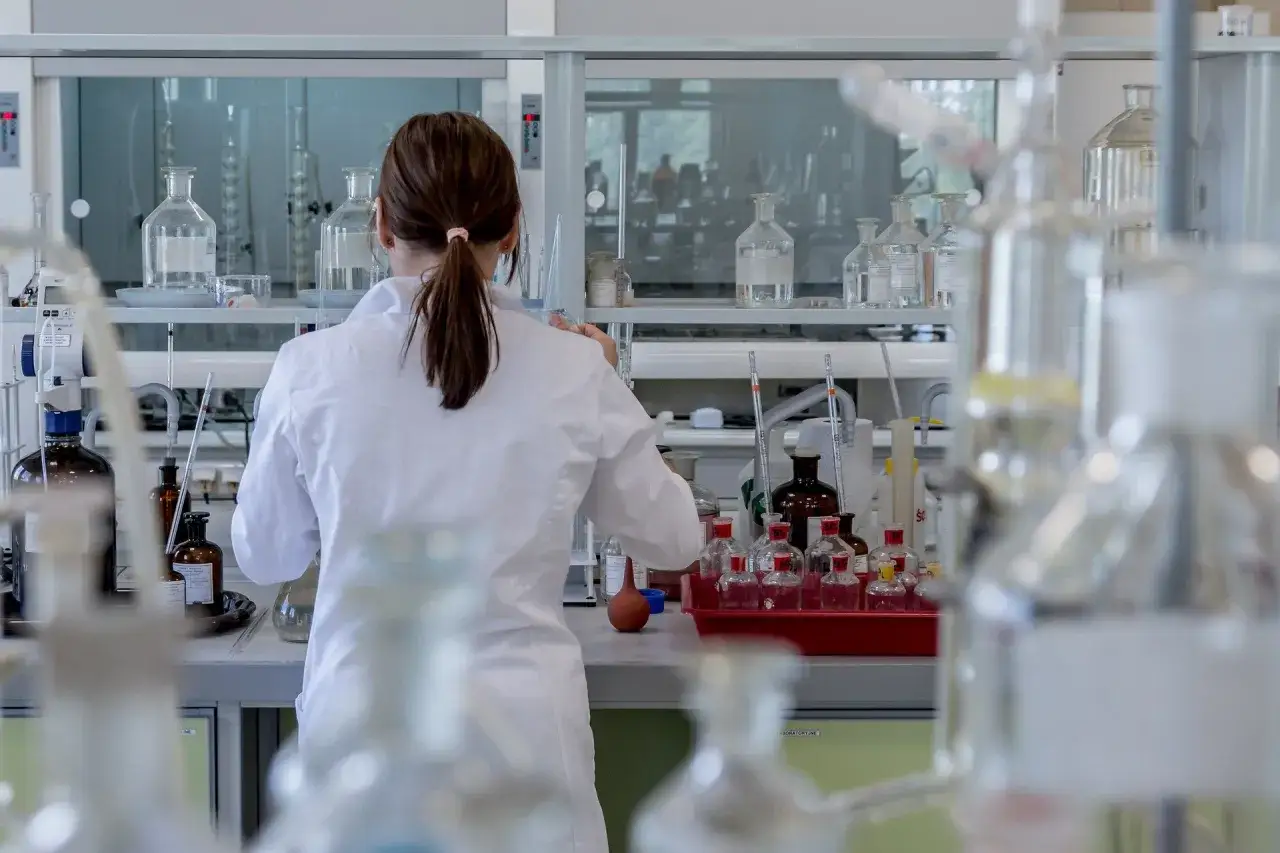 Ricerca offerte di lavoro tecnico di laboratorio biomedico: donna in camice bianco lavora tra provette e becher in un laboratorio moderno.