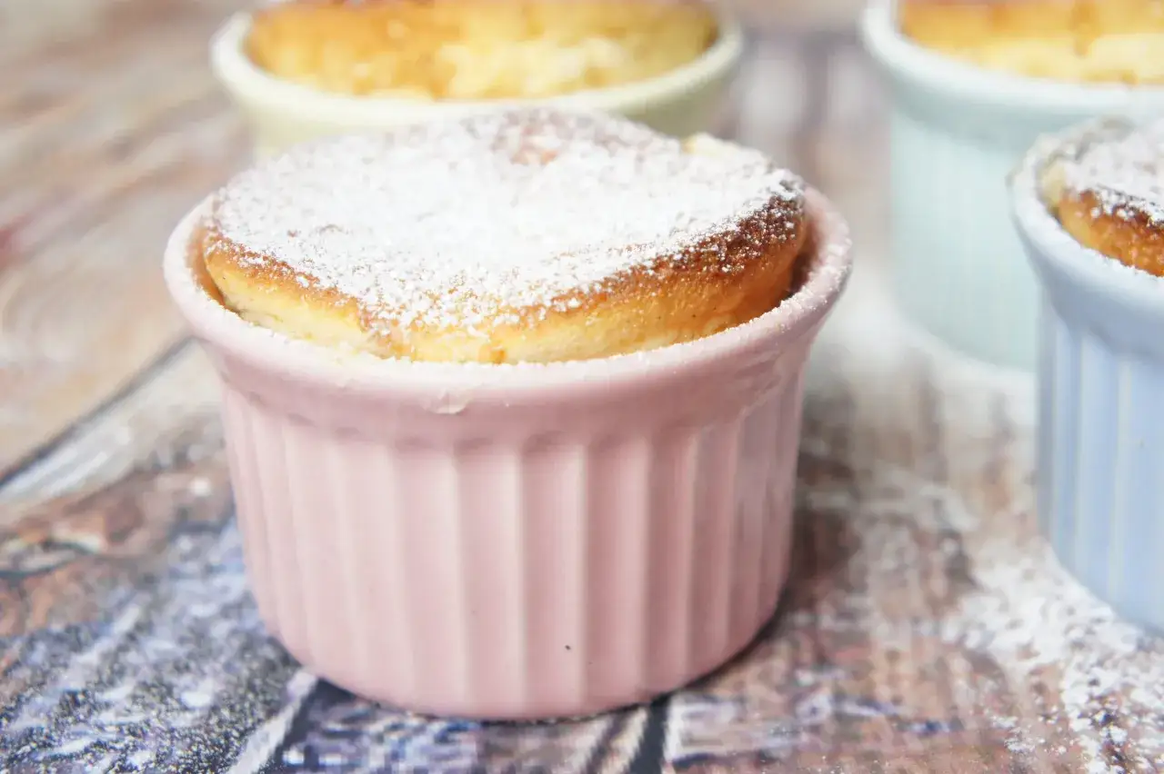Delicioso souffle de vainilla recién horneado, espolvoreado con azúcar glas, en un cuenco rosa.