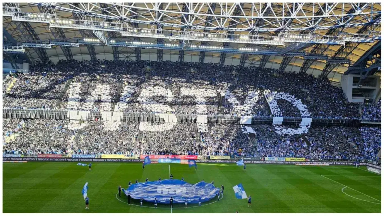 Trybuna stadionu wypełniona kibicami Lecha Poznań tworzącymi napis 