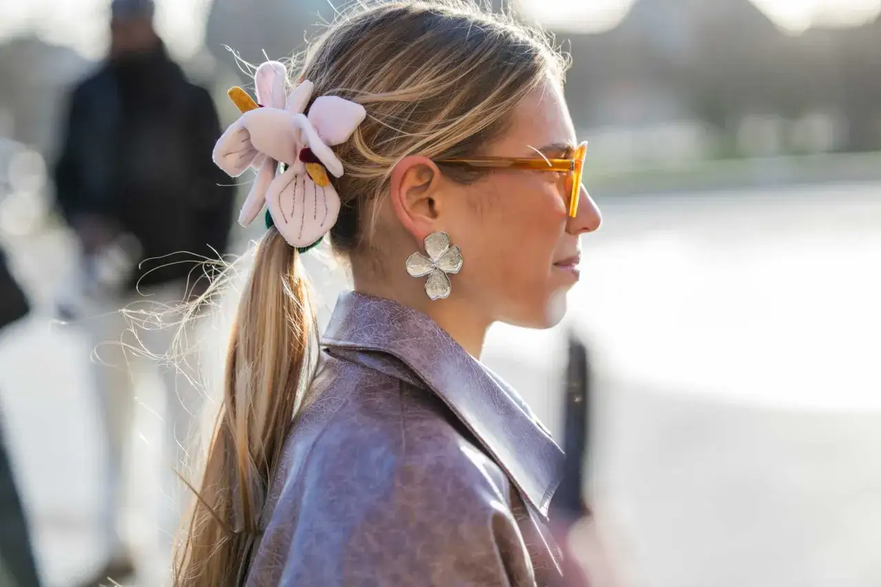Mujer con peinado cola de caballo adornado con una flor de tela y pendientes de pétalos.